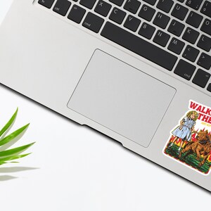 May include: A sticker featuring a cartoon illustration of a girl walking three dogs. The sticker is on a silver laptop. The sticker has the text "Walking the Dog" and "Don't get people on fire".