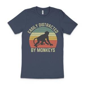 May include: A navy blue t-shirt with a vintage-style graphic of a monkey and the text "Easily Distracted By Monkeys".