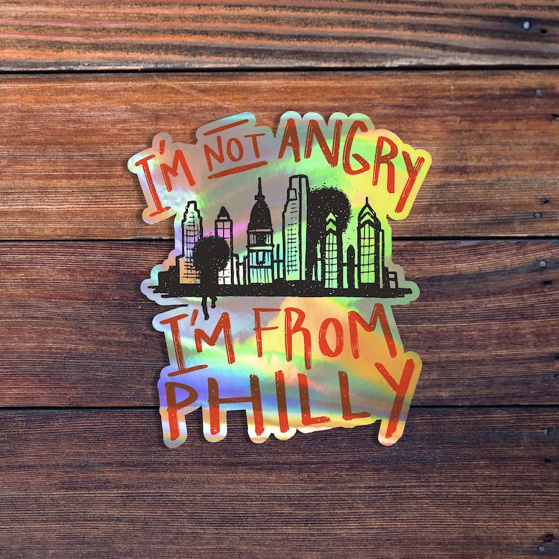 May include: A holographic sticker with the text "I'm not angry I'm from Philly" and a black and white silhouette of the Philadelphia skyline.