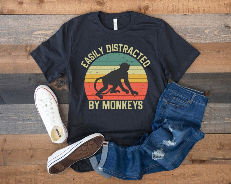 May include: A black t-shirt with a vintage-style graphic of a monkey and the text "Easily Distracted By Monkeys".