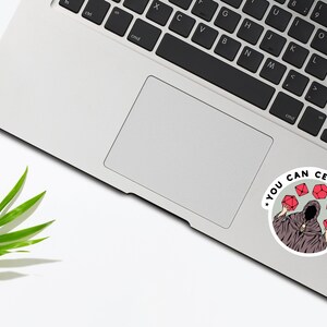 May include: A sticker with a black and white illustration of a hooded figure holding red dice. The text around the figure reads "You can certainly try."