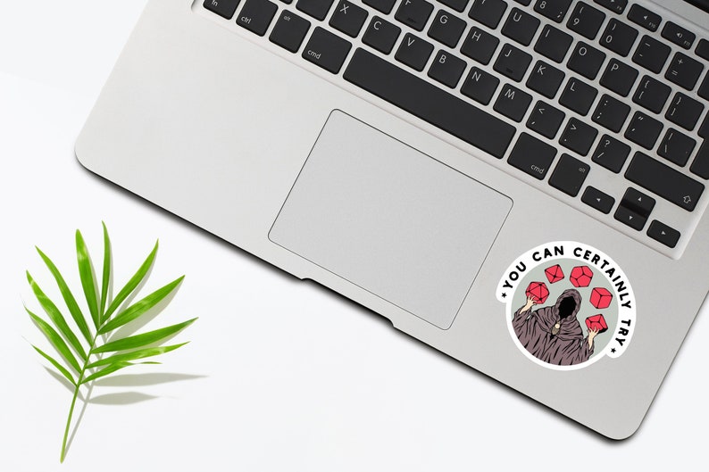 May include: A sticker with a black and white illustration of a hooded figure holding red dice. The text around the figure reads "You can certainly try."