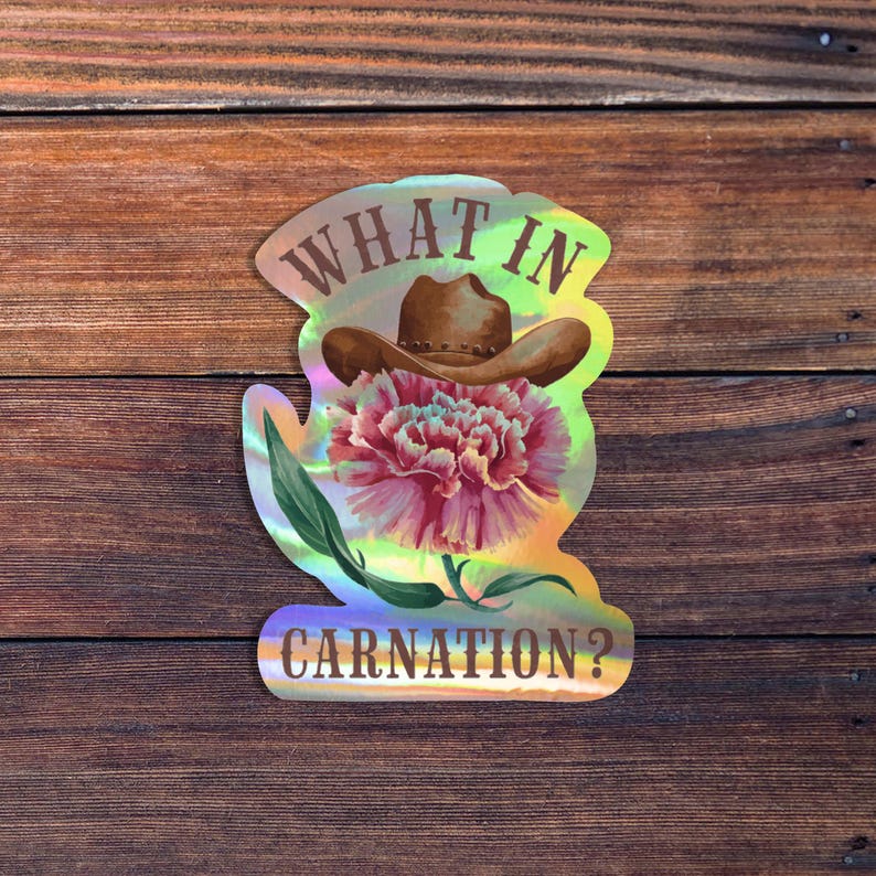 Op de afbeelding: Holografische sticker met een cowboyhoed boven een roze anjerbloem. De tekst "WHAT IN CARNATION?" staat in een speels lettertype. De sticker is geplaatst op een houten achtergrond.