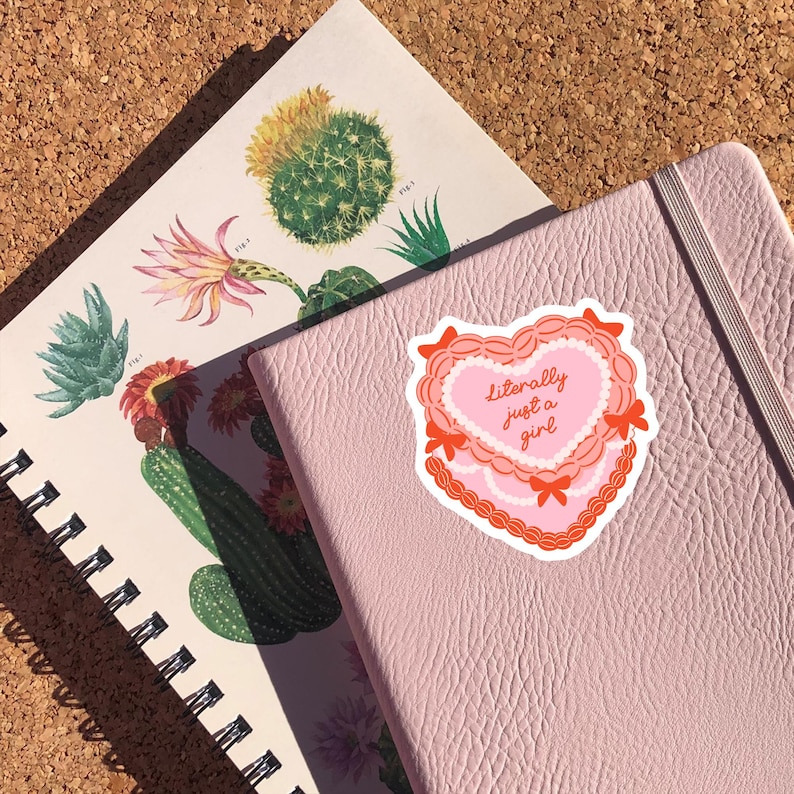 May include: Pink notebook with a heart-shaped sticker that says "literally just a girl" in white text.