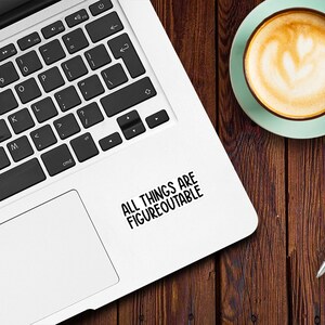 May include: A white laptop computer with a black keyboard and a black and white sticker that says "ALL THINGS ARE FIGUREOUTABLE" on the top right corner of the laptop.