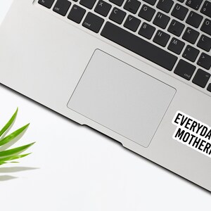 Puede incluir: Un ordenador port&aacute;til blanco con un teclado negro y una pegatina que dice "EVERYDAY I'M MOTHERIN'" en la esquina inferior derecha. Una hoja verde se encuentra en la esquina superior izquierda de la imagen.