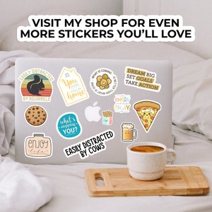 May include: A laptop computer with various stickers on it. The stickers feature cute illustrations and motivational quotes. Some of the stickers include: "Easily Distracted by Squirrels", "You are your home", "What is coming is better than what is gone", "Dream Big Set Goals Take Action", "Okay Okay Okay", "What's stopping you?", "Easily Distracted by Cows", "Enjoy Life".