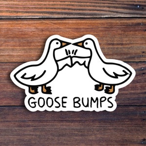 以下が含まれることがあります： 2羽のガチョウが向かい合って描かれた白いステッカー。下に「Goose Bumps」の文字があります。