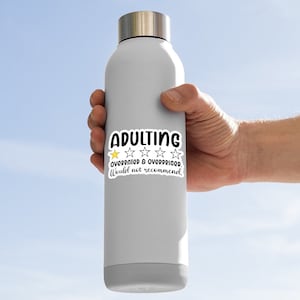May include: A gray insulated water bottle with a silver lid. A white sticker on the bottle reads "ADULTING" in black, with a yellow star and four white stars, and the text "OVERRATED & OVERPRICED. Would not recommend."