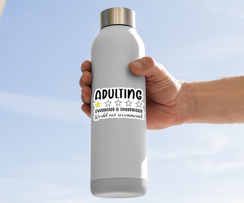 May include: A gray insulated water bottle with a silver lid. A white sticker on the bottle reads "ADULTING" in black, with a yellow star and four white stars, and the text "OVERRATED & OVERPRICED. Would not recommend."