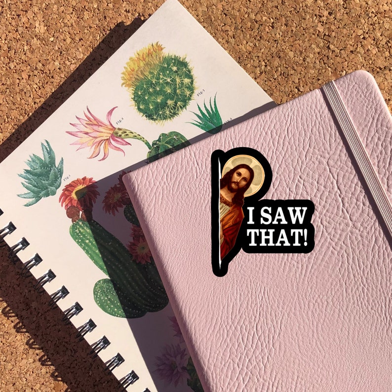 May include: A pink notebook with a sticker of Jesus peeking out from behind a film reel. The sticker says "I saw that!"