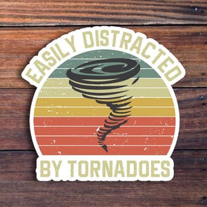 May include: A white sticker with a vintage-style design featuring a tornado and the text "Easily Distracted by Tornadoes".