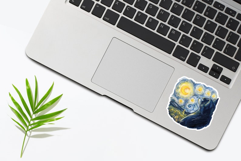 K&ouml;nnte beinhalten: Ein Laptop mit einem Aufkleber eines schwarzen Katers, der zu einem sternenklaren Nachthimmel aufblickt. Der Aufkleber ist eine Nachbildung des ber&uuml;hmten Gem&auml;ldes "Sternennacht" von Vincent van Gogh.