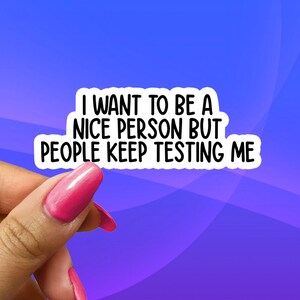 May include: White sticker with black text that reads "I want to be a nice person but people keep testing me". A hand with pink nail polish is holding the sticker.