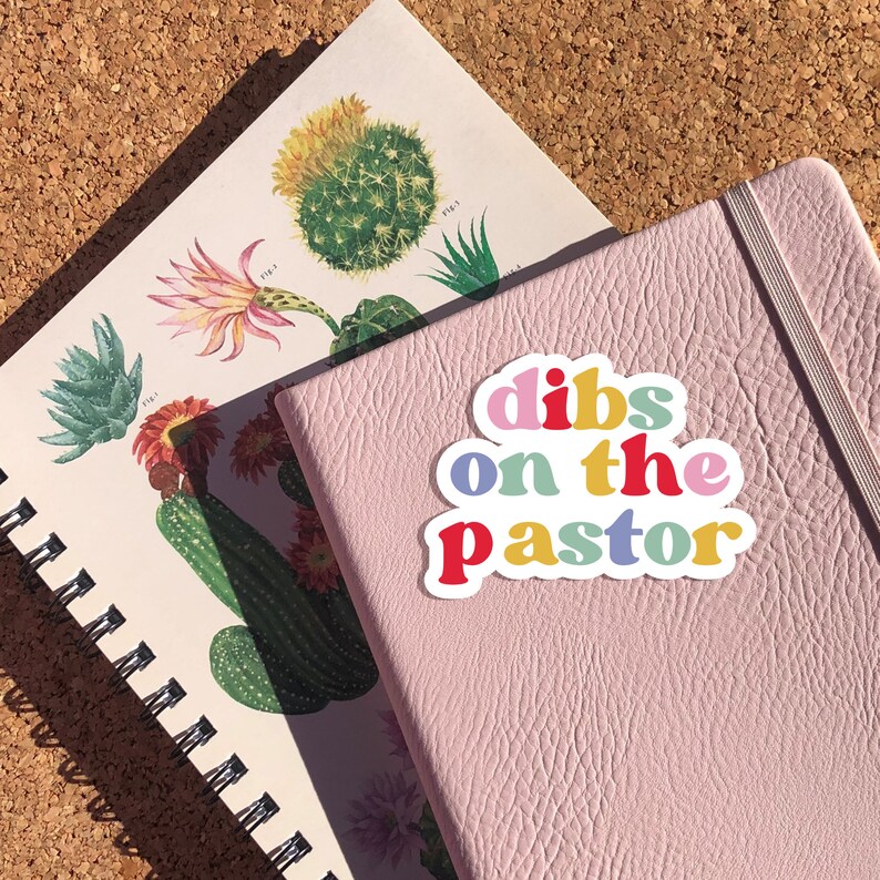 K&ouml;nnte beinhalten: Ein rosa Notizbuch mit einem bunten Aufkleber, auf dem "dibs on the pastor" steht.