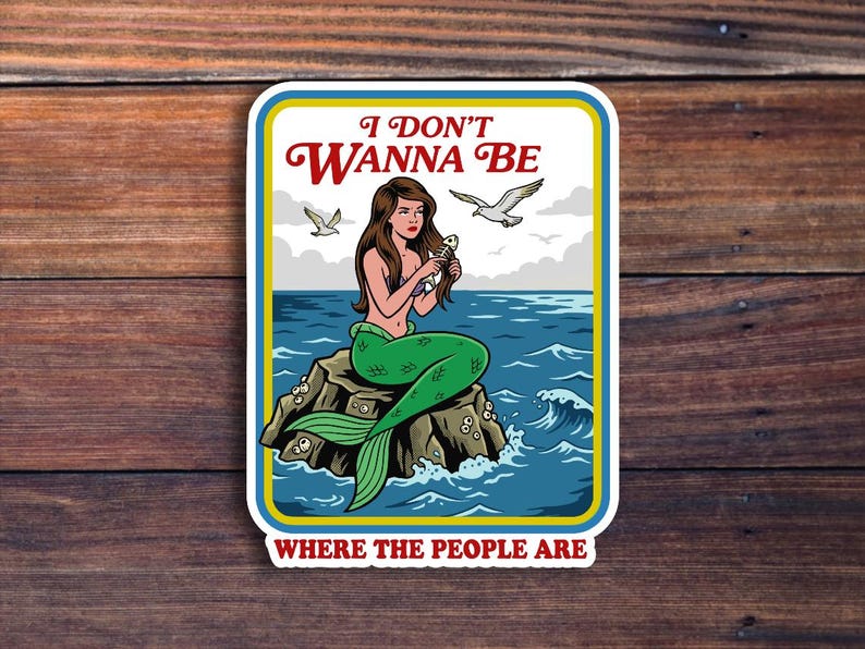 May include: A sticker featuring a mermaid sitting on a rock in the ocean, holding a fish. The sticker has the text "I DON'T WANNA BE WHERE THE PEOPLE ARE" in red and white. The mermaid has green scales and brown hair.