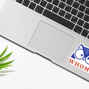 May include: A blue and white owl sticker with the text "WHOM?" in red letters on a silver laptop.