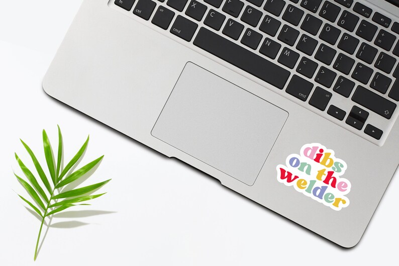May include: A laptop computer with a sticker that says "dibs on the welder" in rainbow colors. The sticker is on the trackpad of the laptop.