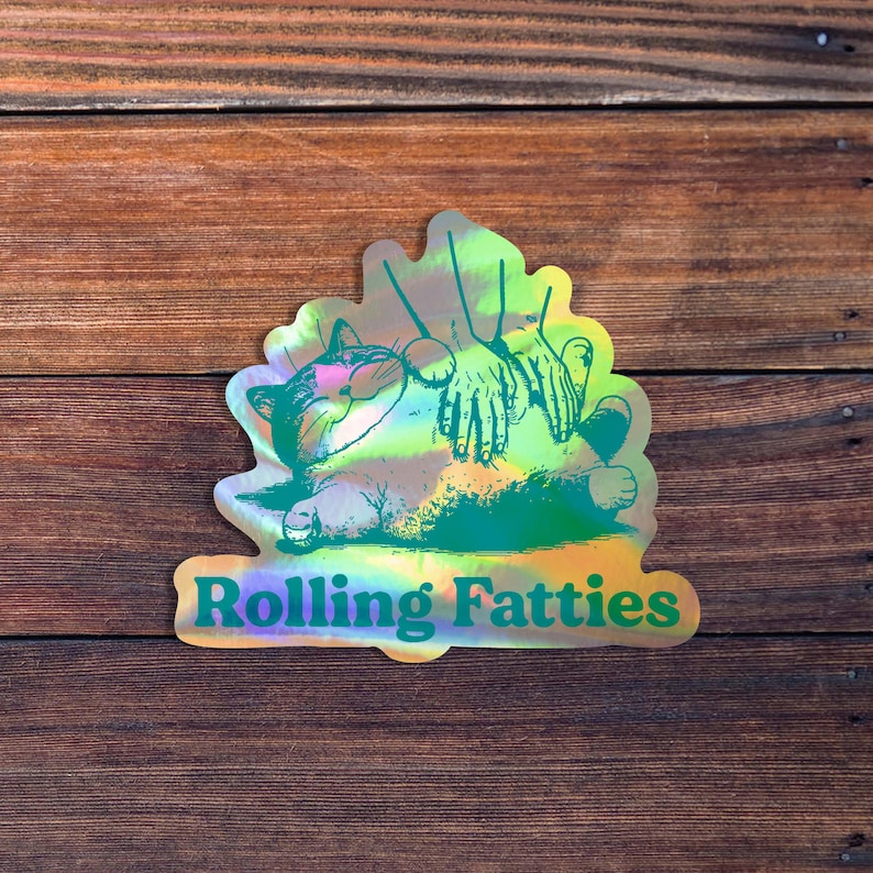 May include: A holographic sticker with a green cartoon cat being rubbed on the belly by two hands. The text "Rolling Fatties" is printed below the cat.