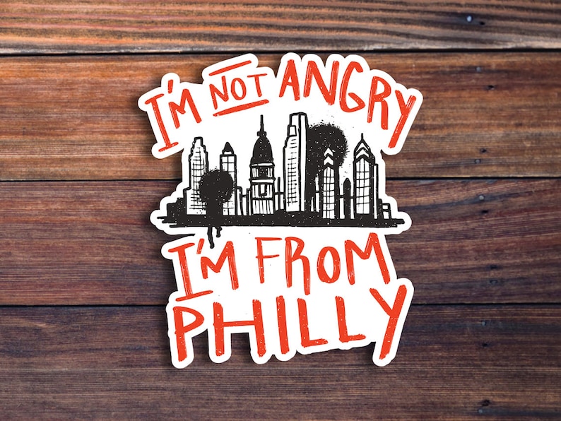 May include: White sticker with black and red text that reads "I'm not angry I'm from Philly" with a black and white illustration of the Philadelphia skyline.