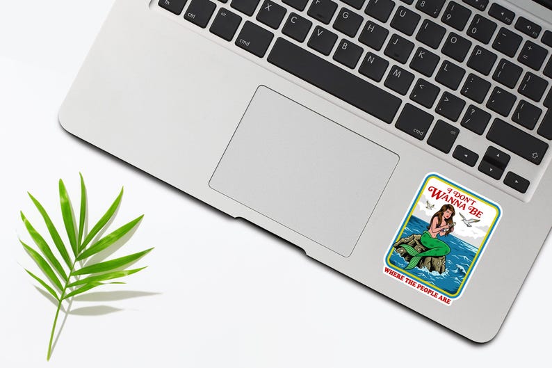 May include: A sticker featuring a mermaid sitting on a rock with the text "I DON'T WANNA BE WHERE THE PEOPLE ARE." The mermaid has long brown hair and a green tail. The sticker is on a laptop.