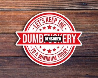 May include: A round white sticker with red accents and text. The sticker reads "LET'S KEEP THE DUMB CENSORED ERY TO A MINIMUM TODAY" in a circular and banner format. The sticker is on a wooden background.