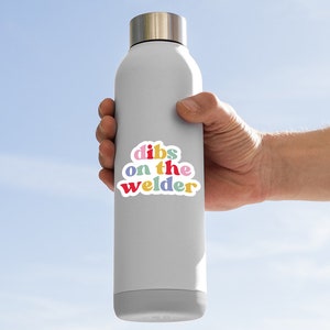 May include: A gray water bottle with a colorful sticker that says "dibs on the welder".