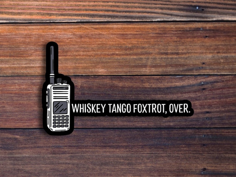 May include: A black and white sticker featuring a walkie-talkie design with the text "WHISKEY TANGO FOXTROT, OVER." The sticker is set against a wooden background.