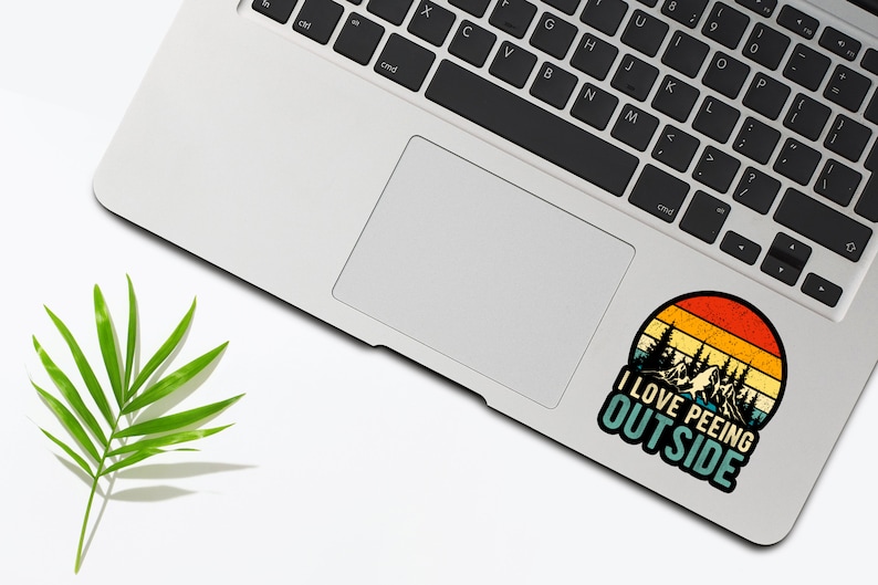 May include: A vintage-style sticker with a sunset background and a silhouette of trees. The sticker says "I love peeing outside". The sticker is on a silver laptop.
