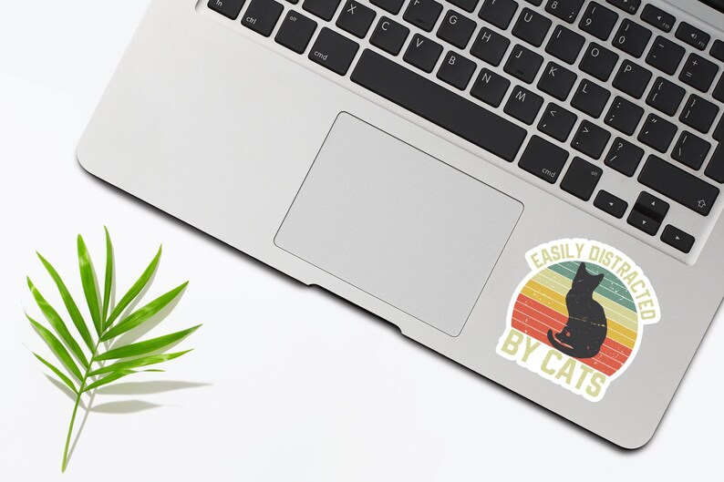 May include: A vintage-style sticker with a black cat silhouette and the text "Easily Distracted By Cats". The sticker has a red, orange, and yellow color scheme.
