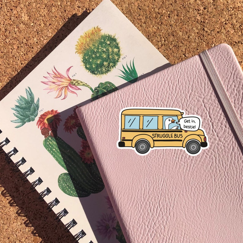 May include: A yellow school bus sticker with a white goose driving. The bus says "STRUGGLE BUS" and the goose has a speech bubble that says "Get in, bestie!"