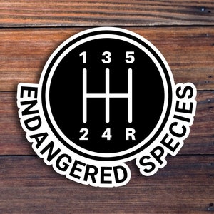 May include: A black and white sticker with a gear shift pattern and the text "ENDANGERED SPECIES" around the outside.