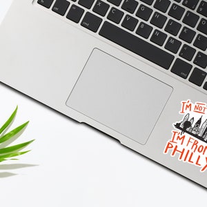 May include: A laptop computer with a sticker on the trackpad that says "I'm not angry I'm from Philly" with a black and white illustration of the Philadelphia skyline.