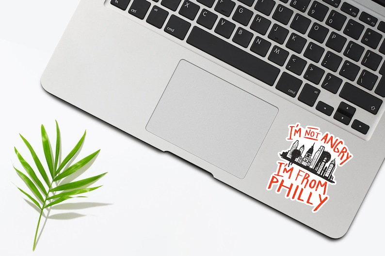 May include: A laptop computer with a sticker on the trackpad that says "I'm not angry I'm from Philly" with a black and white illustration of the Philadelphia skyline.