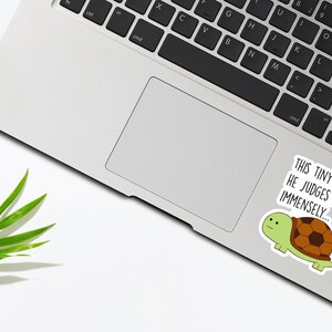 May include: A sticker with a cartoon turtle on a laptop. The sticker says "This tiny turtle... He judges you immensely..."