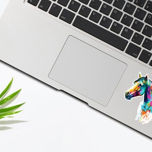 May include: A colorful abstract watercolor painting of a horse's head on a white sticker. The sticker is placed on a silver laptop.