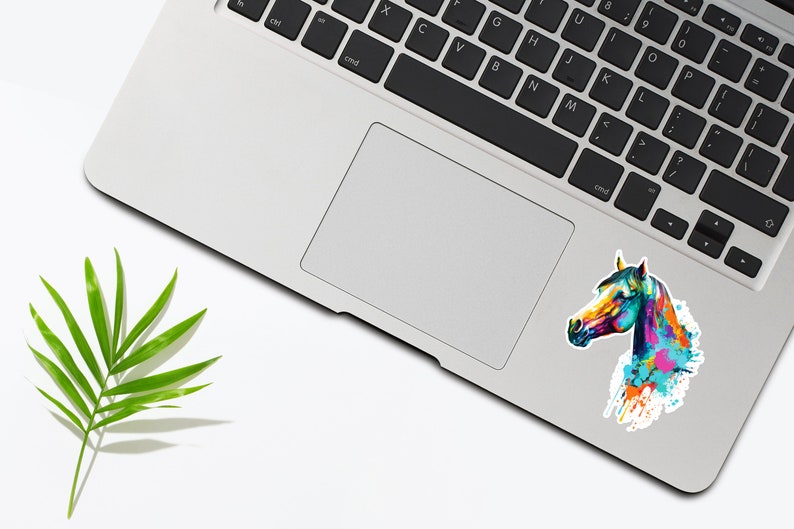 May include: A colorful abstract watercolor painting of a horse's head on a white sticker. The sticker is placed on a silver laptop.