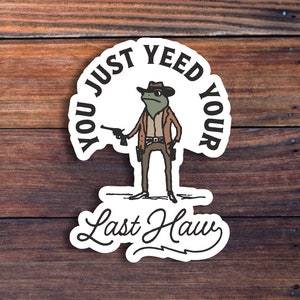 May include: A white sticker with a cartoon frog wearing a cowboy hat and holding a gun. The text on the sticker reads "You just yeed your last haw".
