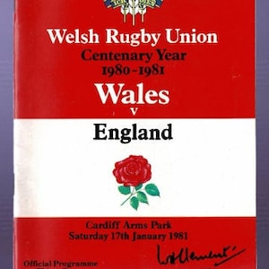 Könnte beinhalten: Ein rot-weißes Programm für ein Rugby-Spiel zwischen Wales und England. Das Programm zeigt das walisische Nationalemblem, einen roten Drachen, und das englische Nationalemblem, eine rote Rose. Das Spiel fand am 17. Januar 1981 im Cardiff Arms Park statt.