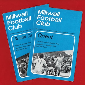 Peut inclure: Deux programmes de match vintage du Millwall Football Club. Les couvertures bleues présentent du texte blanc et une photo d'un match de football. L'un est pour Bristol City, l'autre pour Orient. Les programmes sont sur fond rouge.
