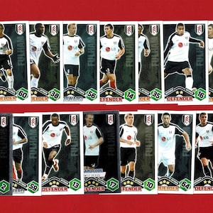 May include: A collection of Fulham football player trading cards. Each card features a player in a white and black uniform, with the Fulham logo. The cards display player names, positions, and ratings. The background is a solid red.