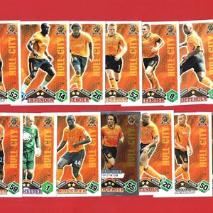 May include: A collection of Hull City football trading cards. The cards feature players in orange and black uniforms, with player names and positions displayed. The background is a gradient of orange and brown.