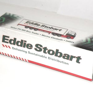 May include: A white rectangular box with the words "Eddie Stobart" in large green letters. The box features a red and white striped border and a graphic of a truck. Text includes "Delivering Sustainable Distribution."