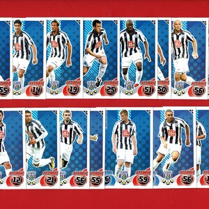 May include: A collection of soccer trading cards featuring players in black and white striped jerseys. Each card displays a player's image, name, and numerical stats against a blue background. The cards are arranged on a red surface.