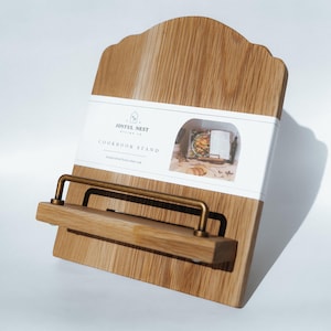 May include: A white ceramic mug with a black handle and the text "But First, Coffee" in a bold, black font. The mug is set against a blurred background, suggesting a cozy setting.