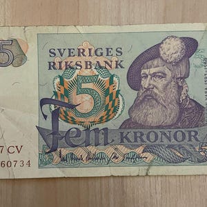 May include: A vintage 5 Swedish Kronor banknote from 1977. The bill features a portrait of Gustav Vasa and the text "Sveriges Riksbank". The number 5 is prominently displayed.