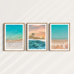 May include: Three framed photographs of a beach scene. The top photo shows a small island with a tree in the middle of the ocean. The middle photo shows the ocean water with a sandy beach below. The bottom photo shows a beach with rows of white umbrellas.