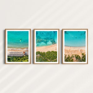 May include: Three framed photographs of aerial views of a beach with turquoise water, white sand, and green vegetation. The beach has a row of colorful umbrellas and chairs.