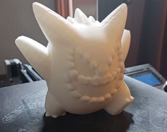 May include: A white 3D printed figurine of a ghost-like Pokemon character with a jagged, toothy grin. The figurine is posed with its arms raised and its legs spread apart.