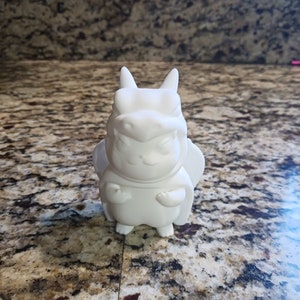May include: White ceramic figurine of a dragon with a fierce expression. The dragon is standing on a granite countertop.